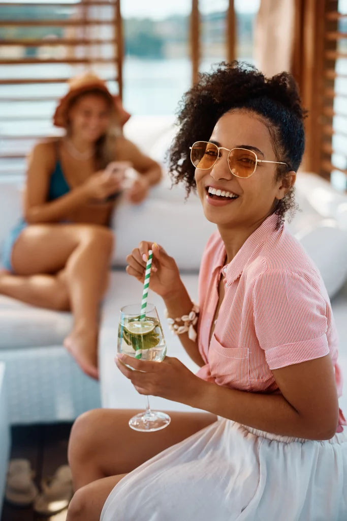 Two women sitting on a couch enjoying a drink while planning their vacation with the help of a travel agent.